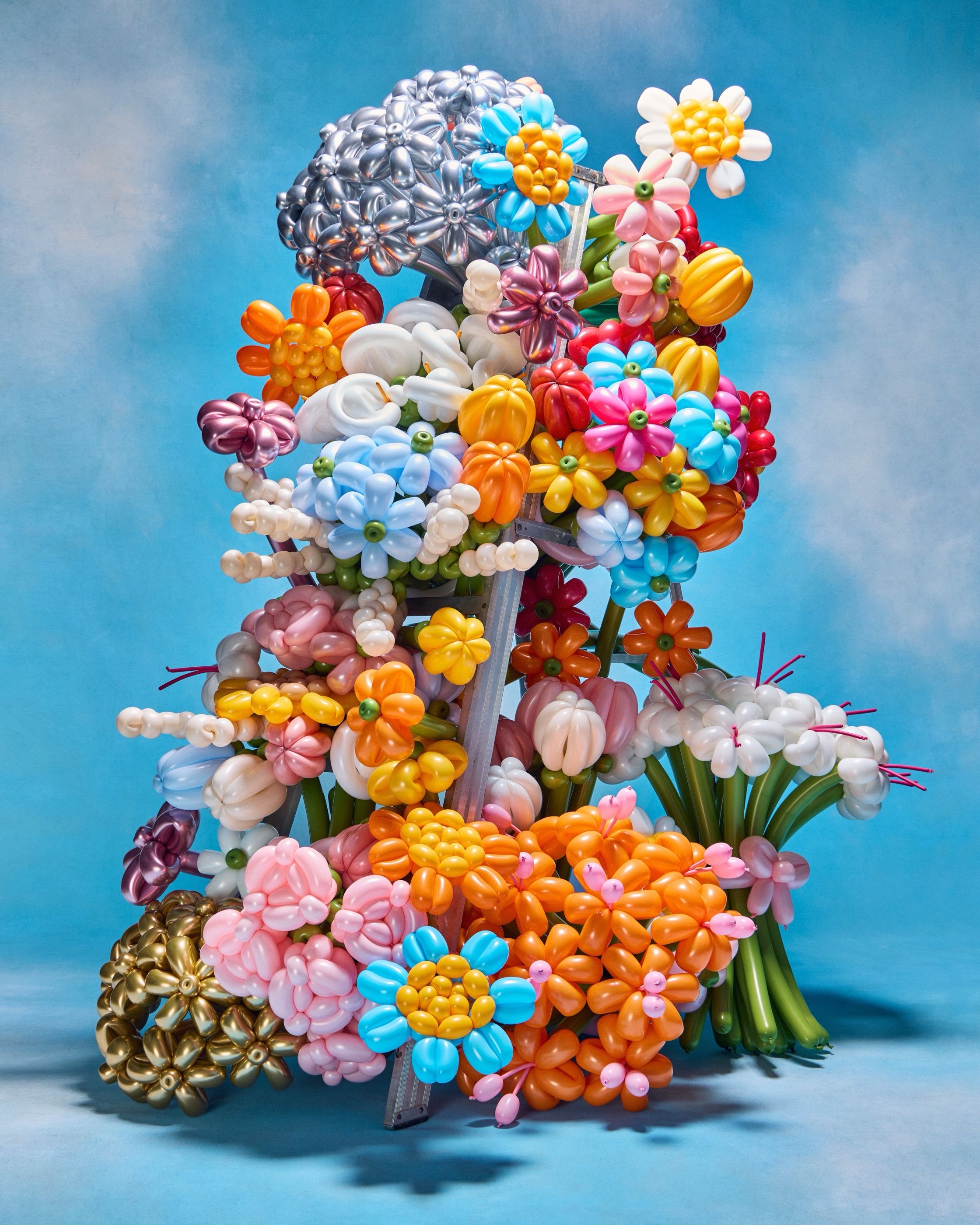 A large sculptural arrangement of balloon flowers in many colors on a ladder frame, against blue.