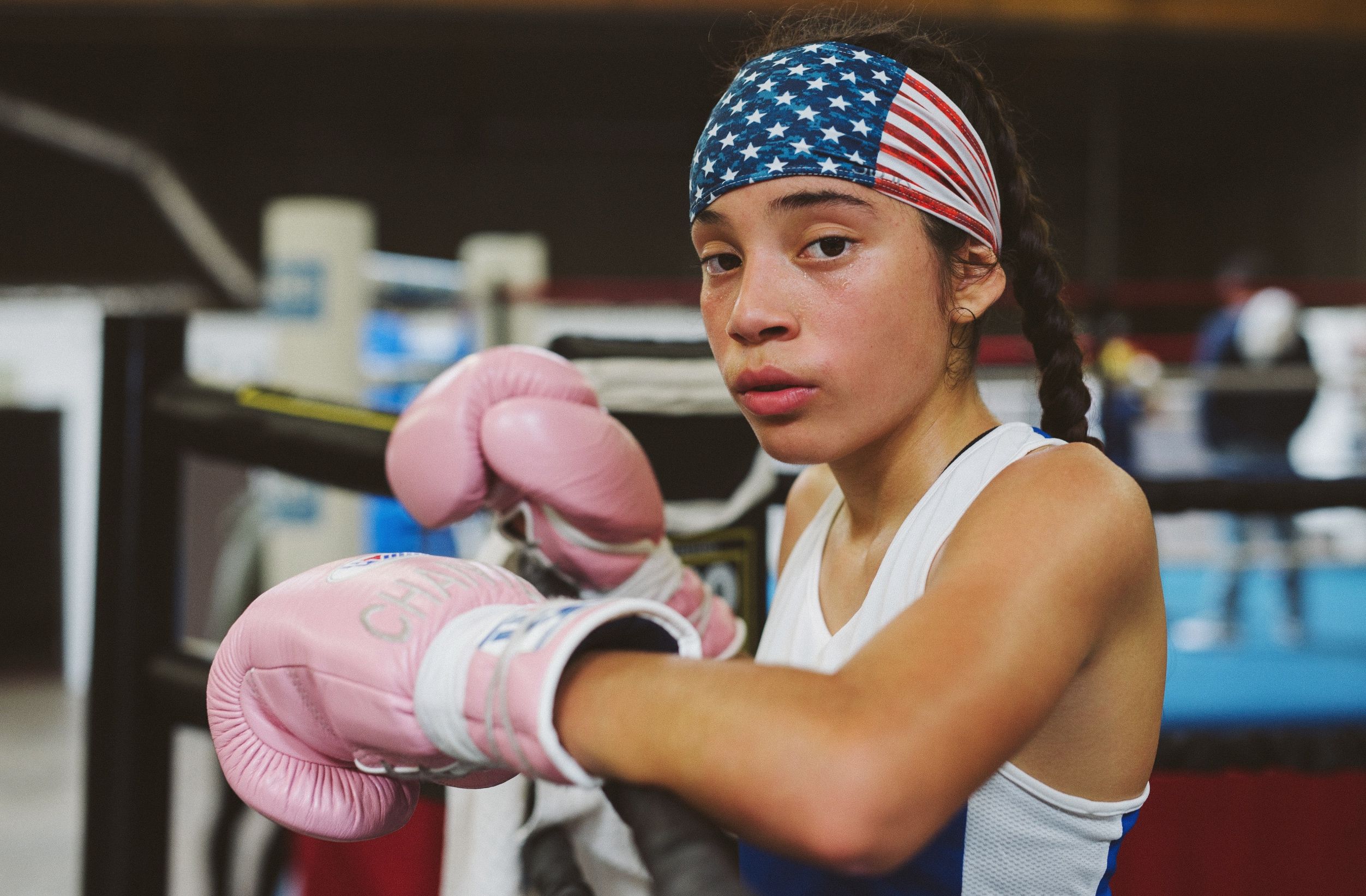 Young boxer wearing pink gloves and a flag-patterned headband stands in a boxing gym.