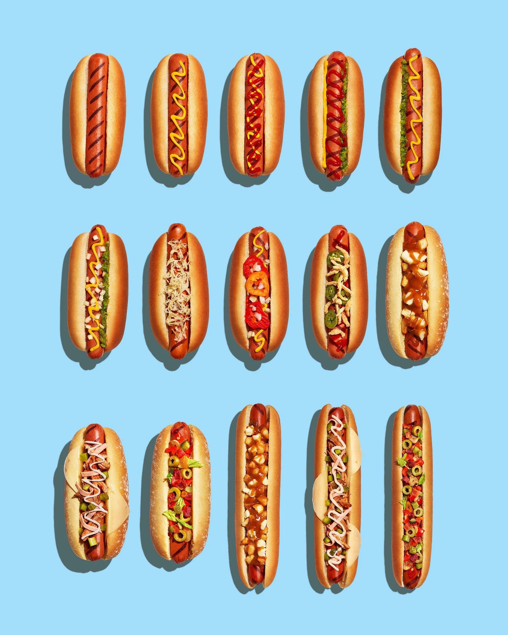 Grid of hot dogs with varied toppings such as ketchup, mustard, onions, olives and peppers on a light blue background.