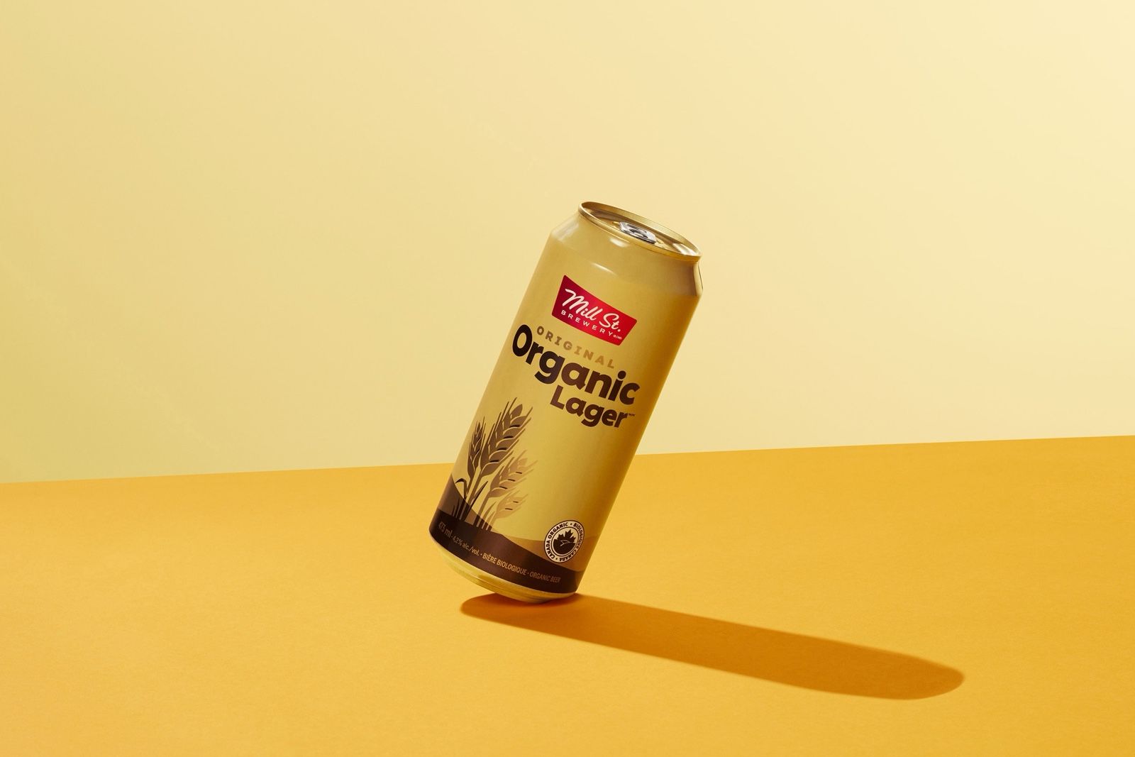 A can of Mill St. Brewery Organic Lager tilted on its edge against a yellow background.