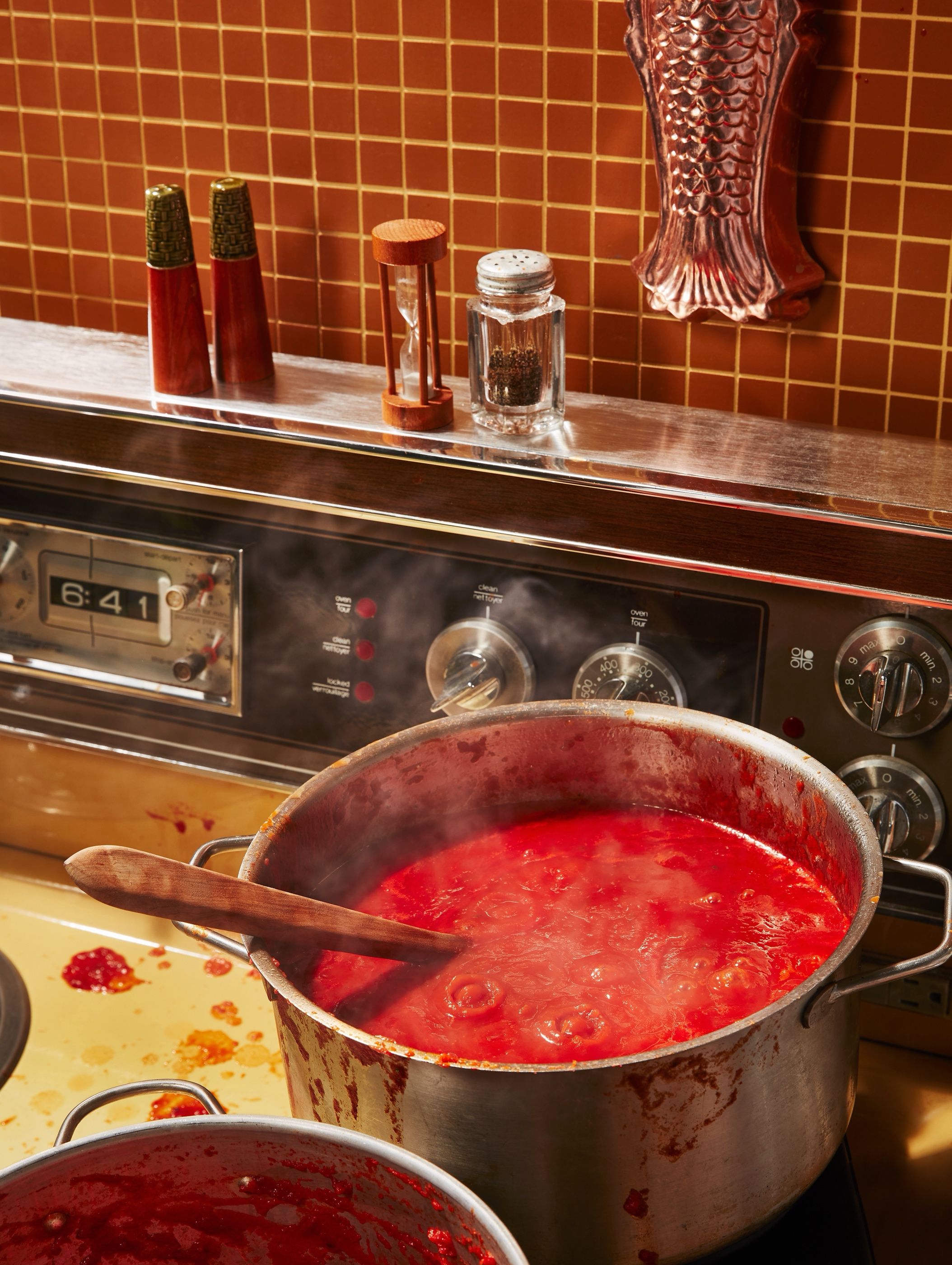 A pot of tomato sauce simmering on a stove in a kitchen with orange tile backsplash and a fish-shaped mold on the wall.