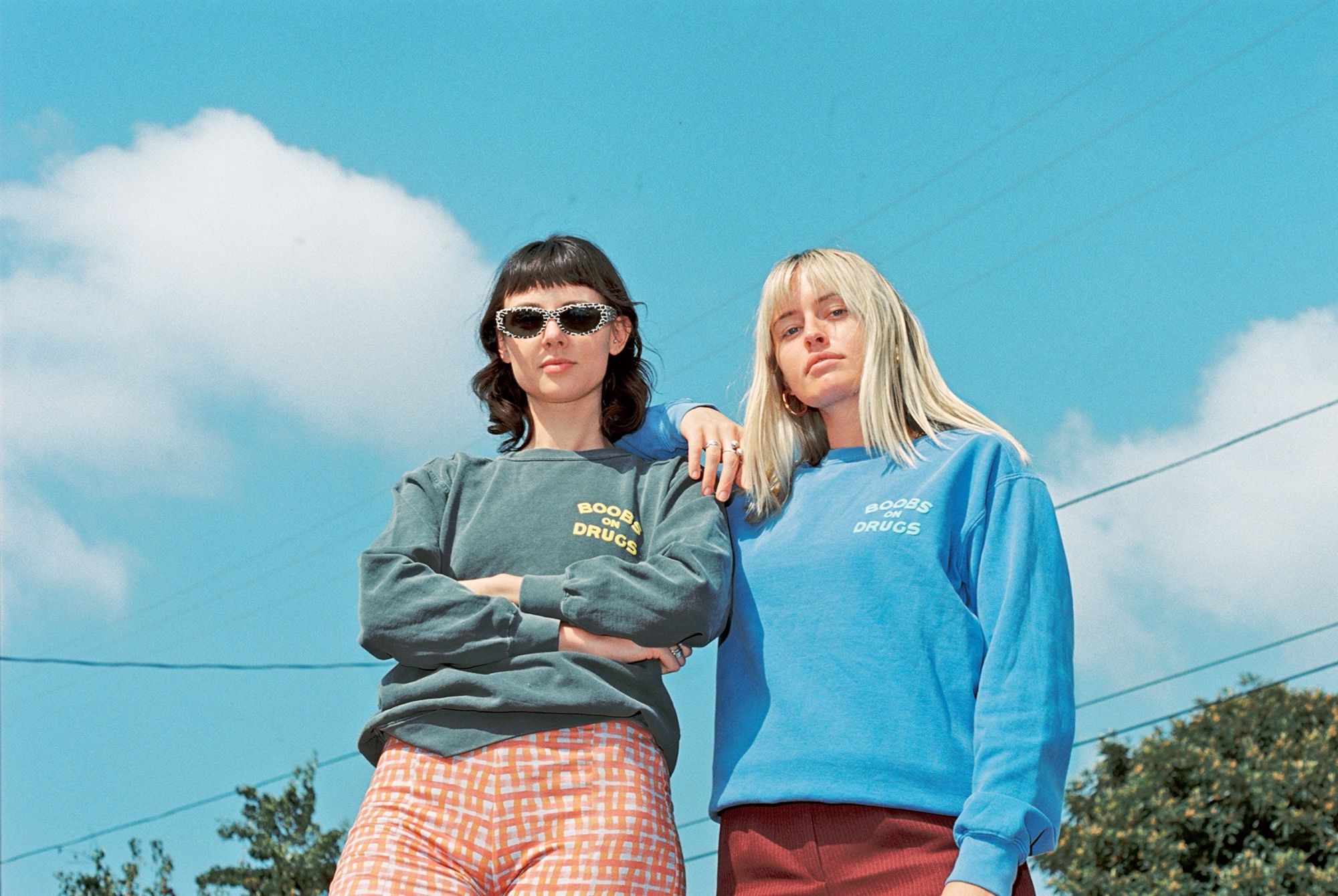 Two women standing outdoors against a blue sky, wearing matching sweatshirts printed with a slogan.