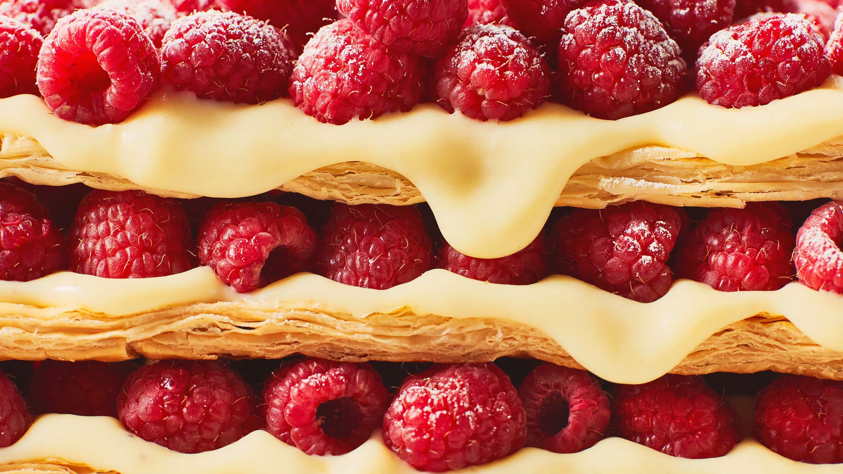 Cross-section of a layered pastry with raspberries and cream between sheets of puff pastry, close-up.