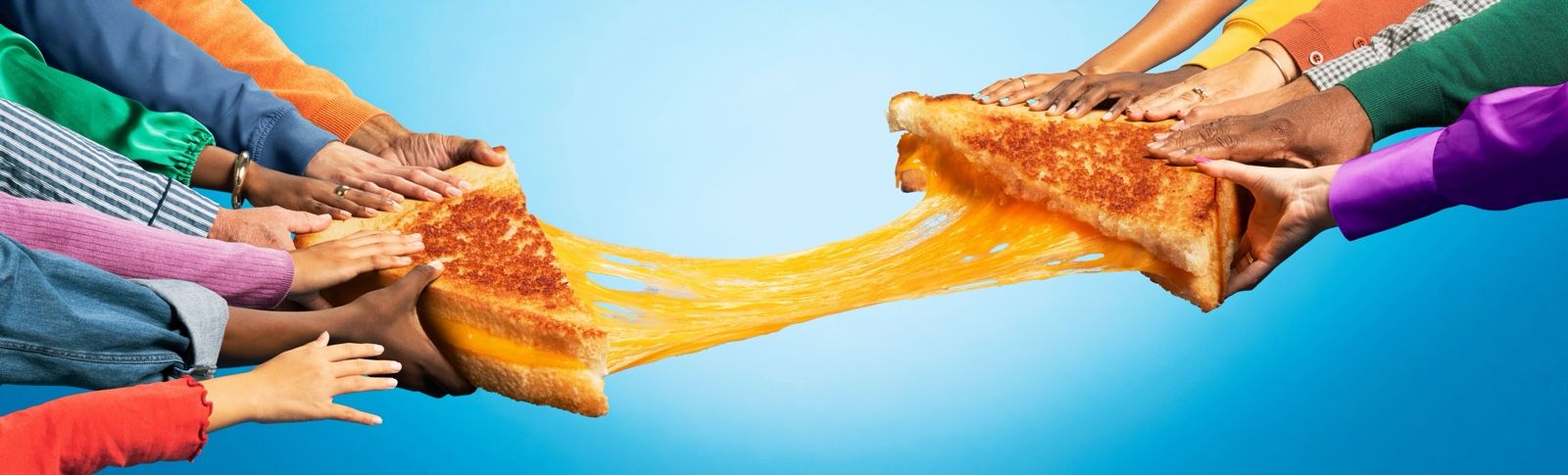 Two grilled cheese sandwich halves pulled apart with a long cheese pull, held by hands on a blue background.
