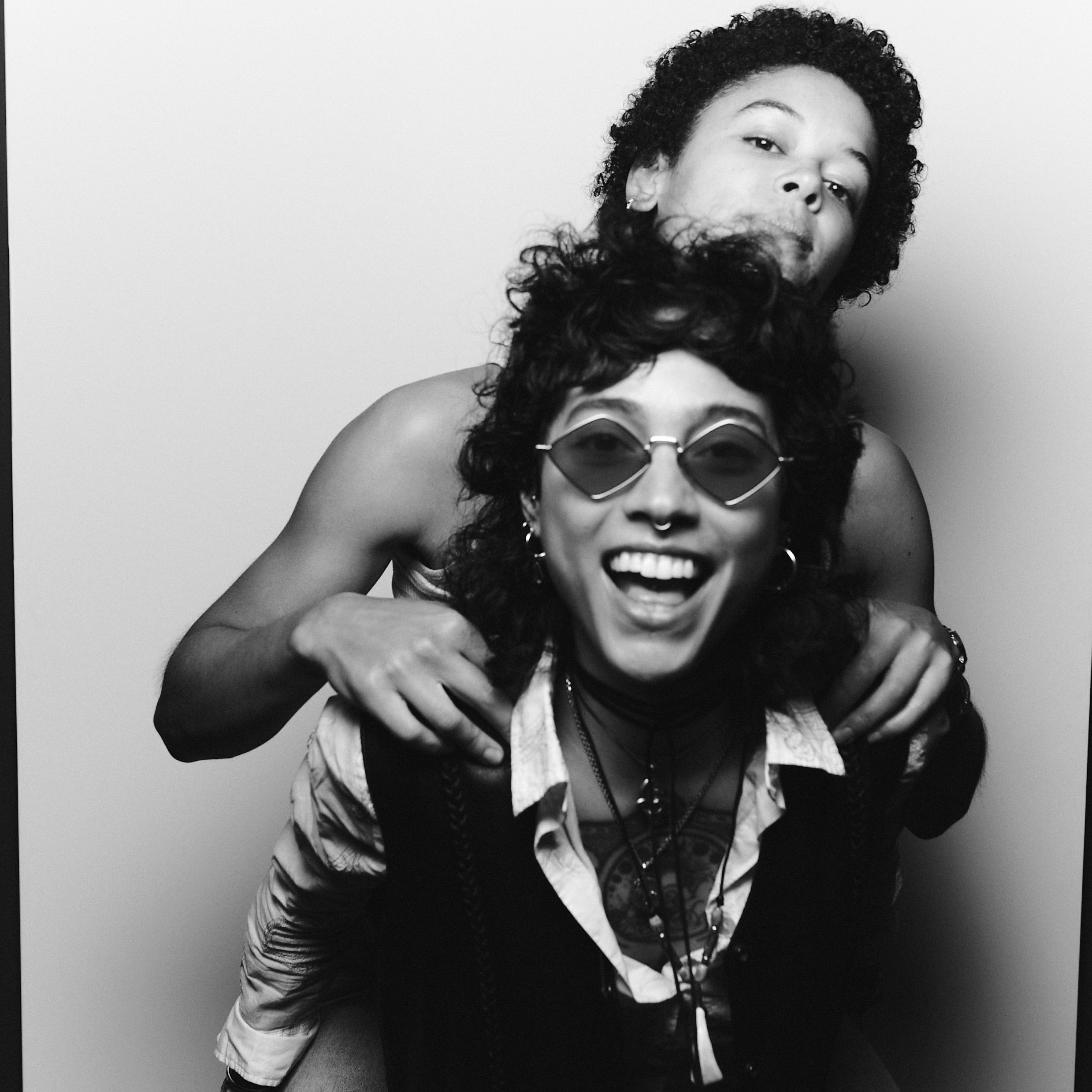 Black-and-white portrait of a couple embracing closely, one wearing a wide-brimmed hat and sunglasses.