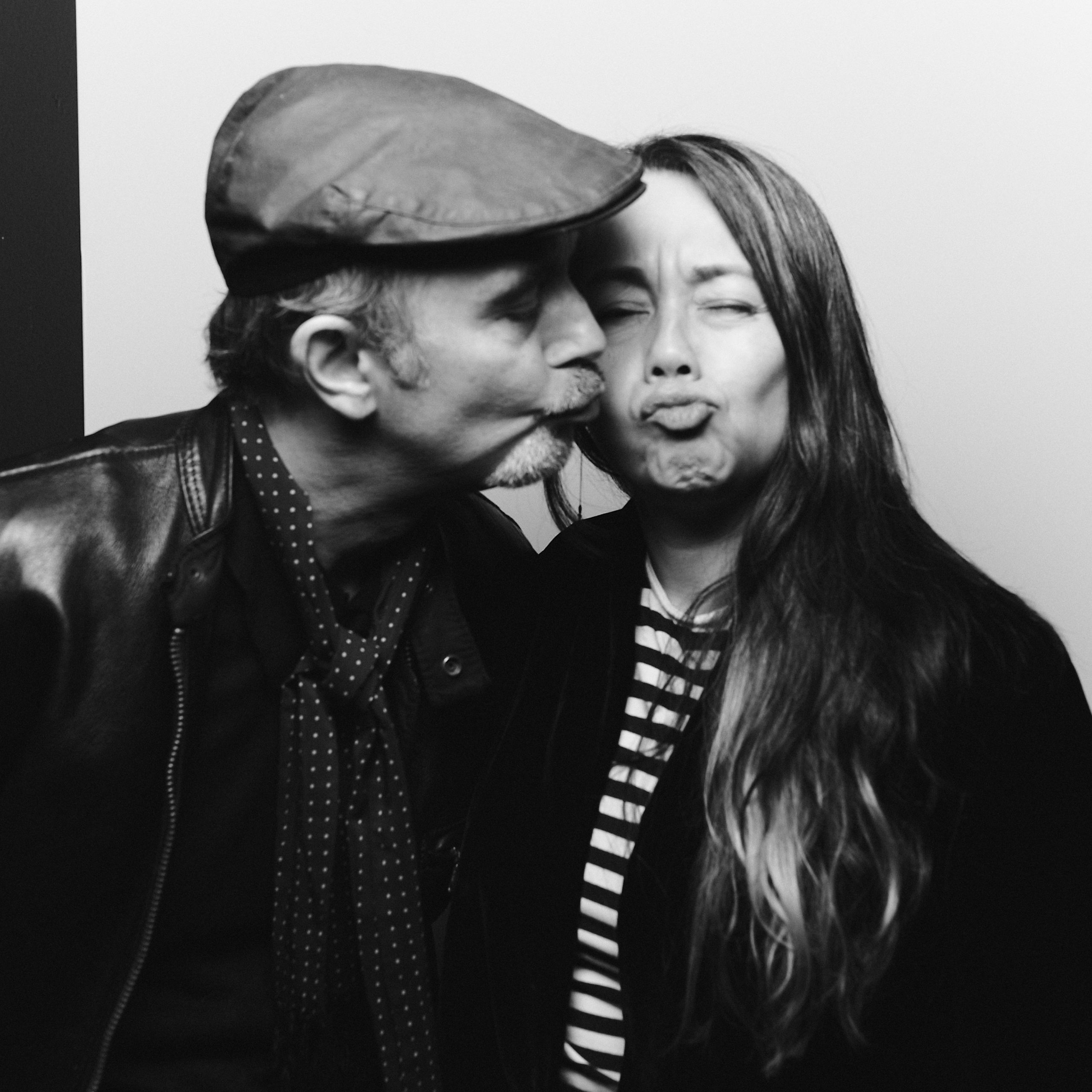 Black-and-white close-up of a man in a flat cap and a woman making playful faces close together.