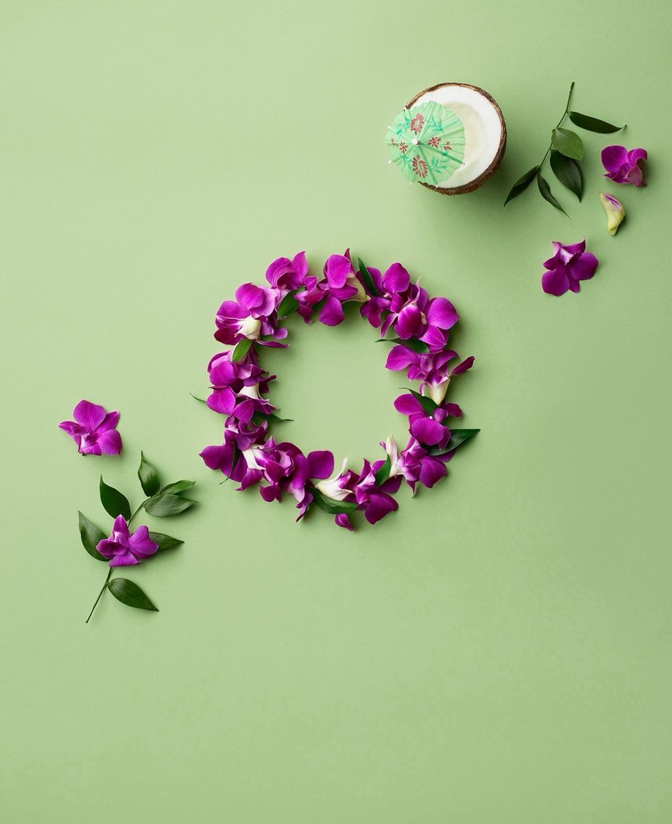 Purple orchid petals arranged in a ring beside a coconut half with a paper drink umbrella on a green background.