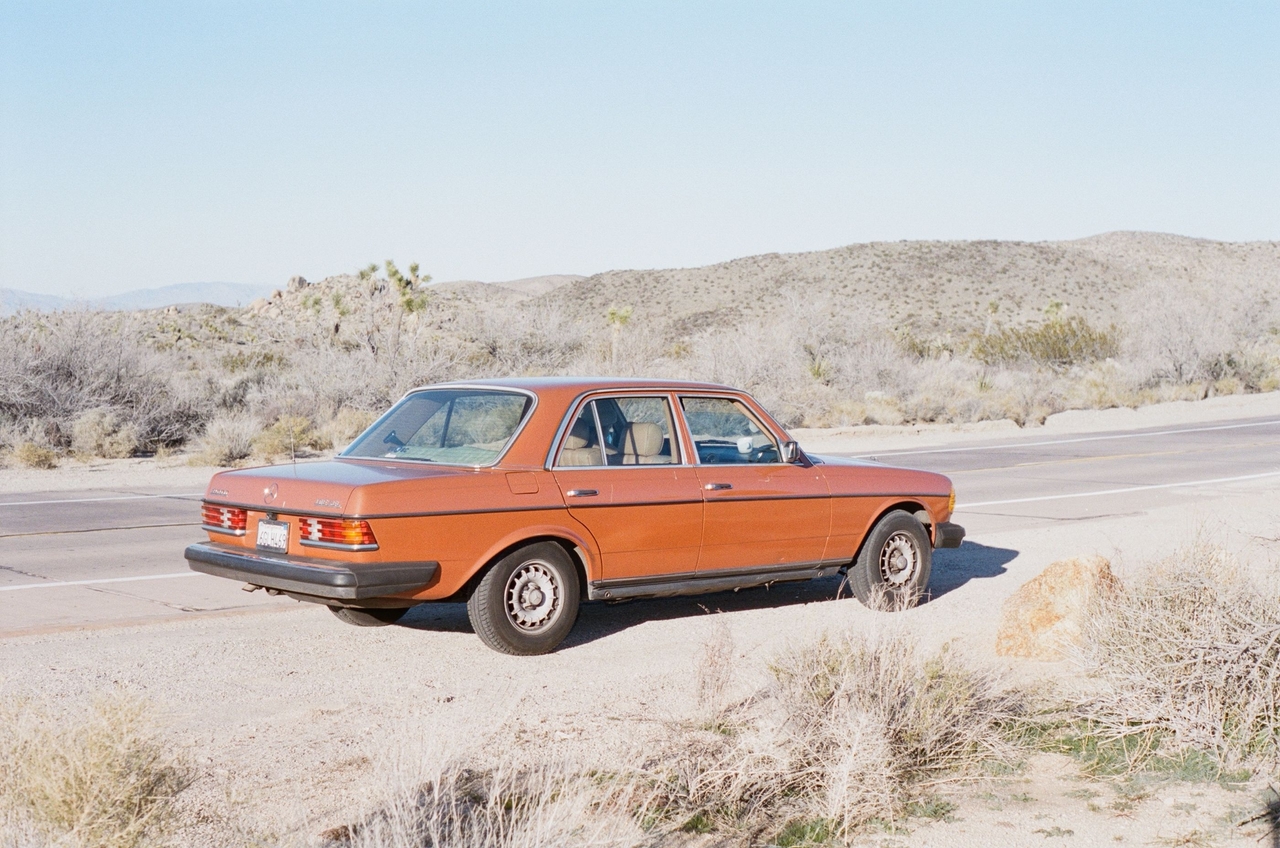 Vintage orange Mercedes-Benz sedan parked on the shoulder of a desert road.