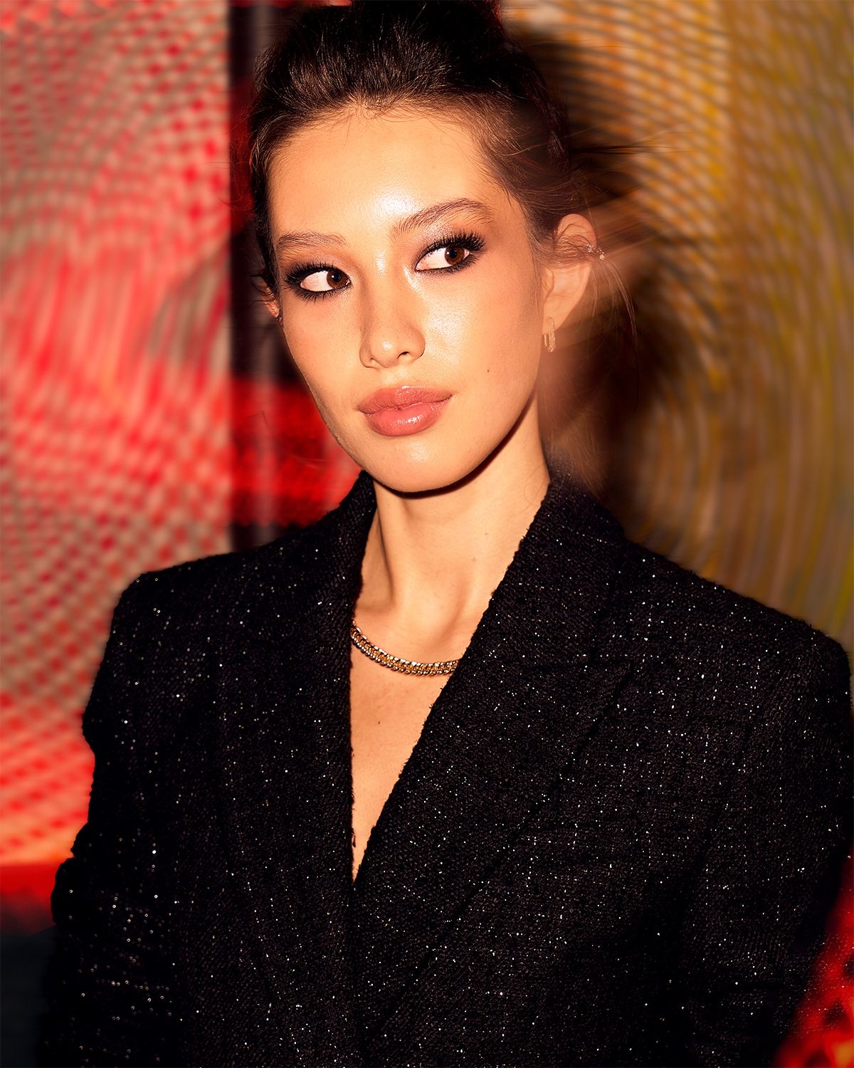 Close-up portrait of a woman in a black sparkly blazer, colorful blurred lights behind her.