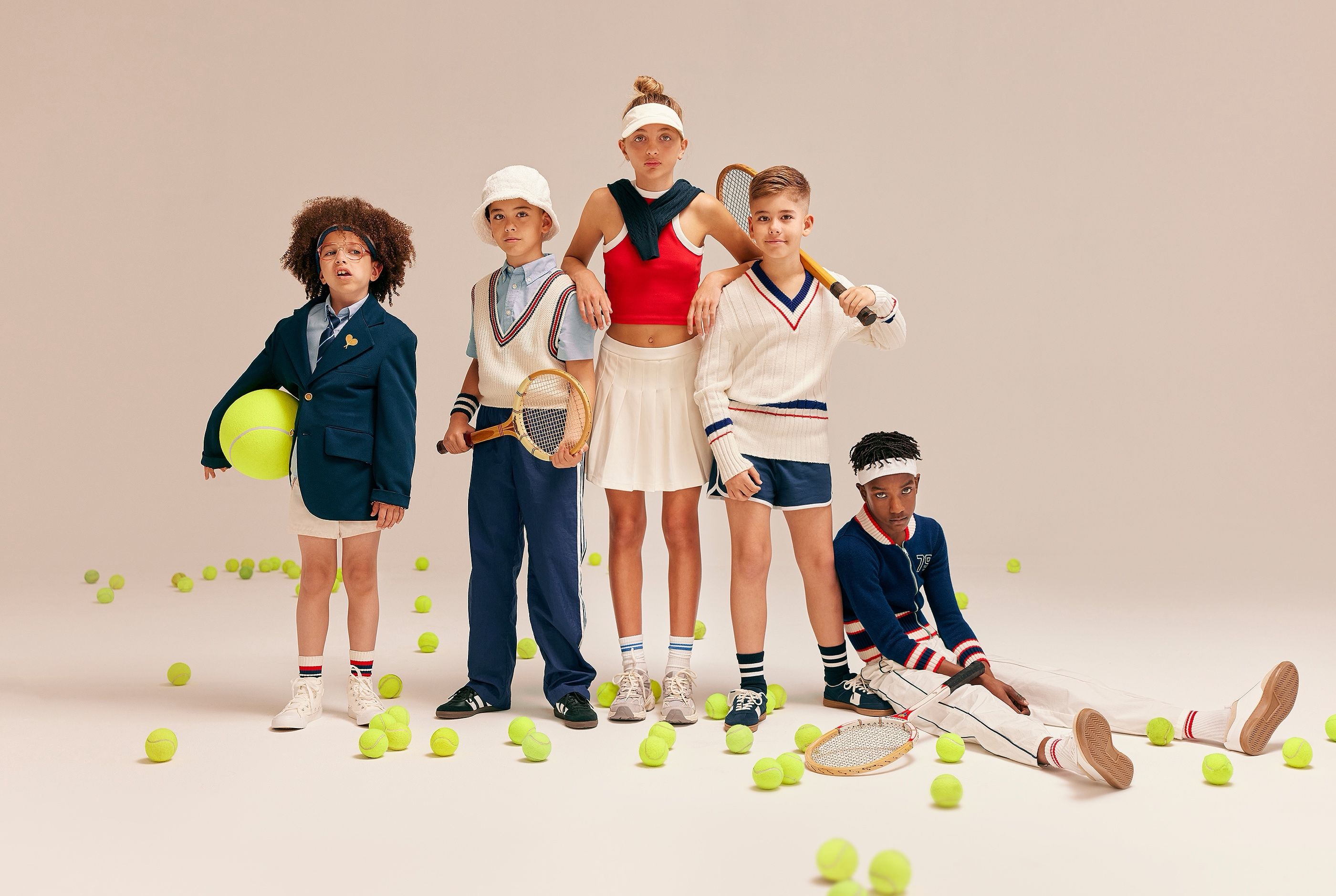 Five children in vintage tennis outfits posing with rackets and scattered tennis balls in a studio.