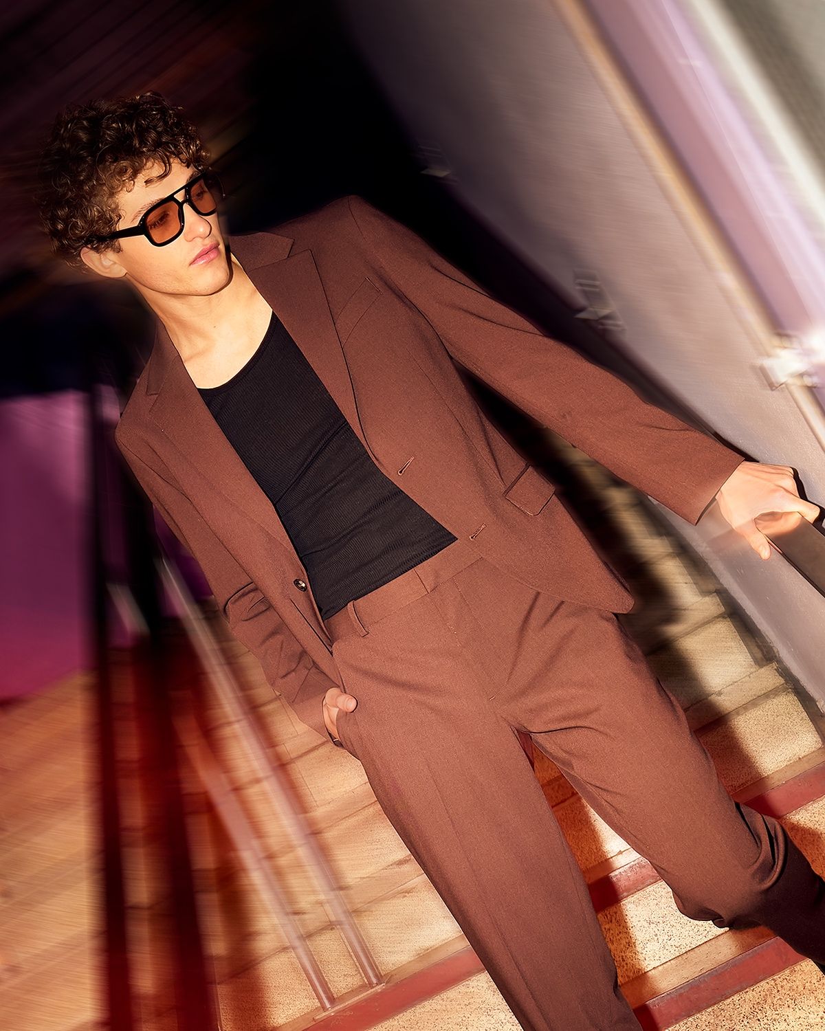 Motion-blurred man in a brown suit and sunglasses descending a staircase.
