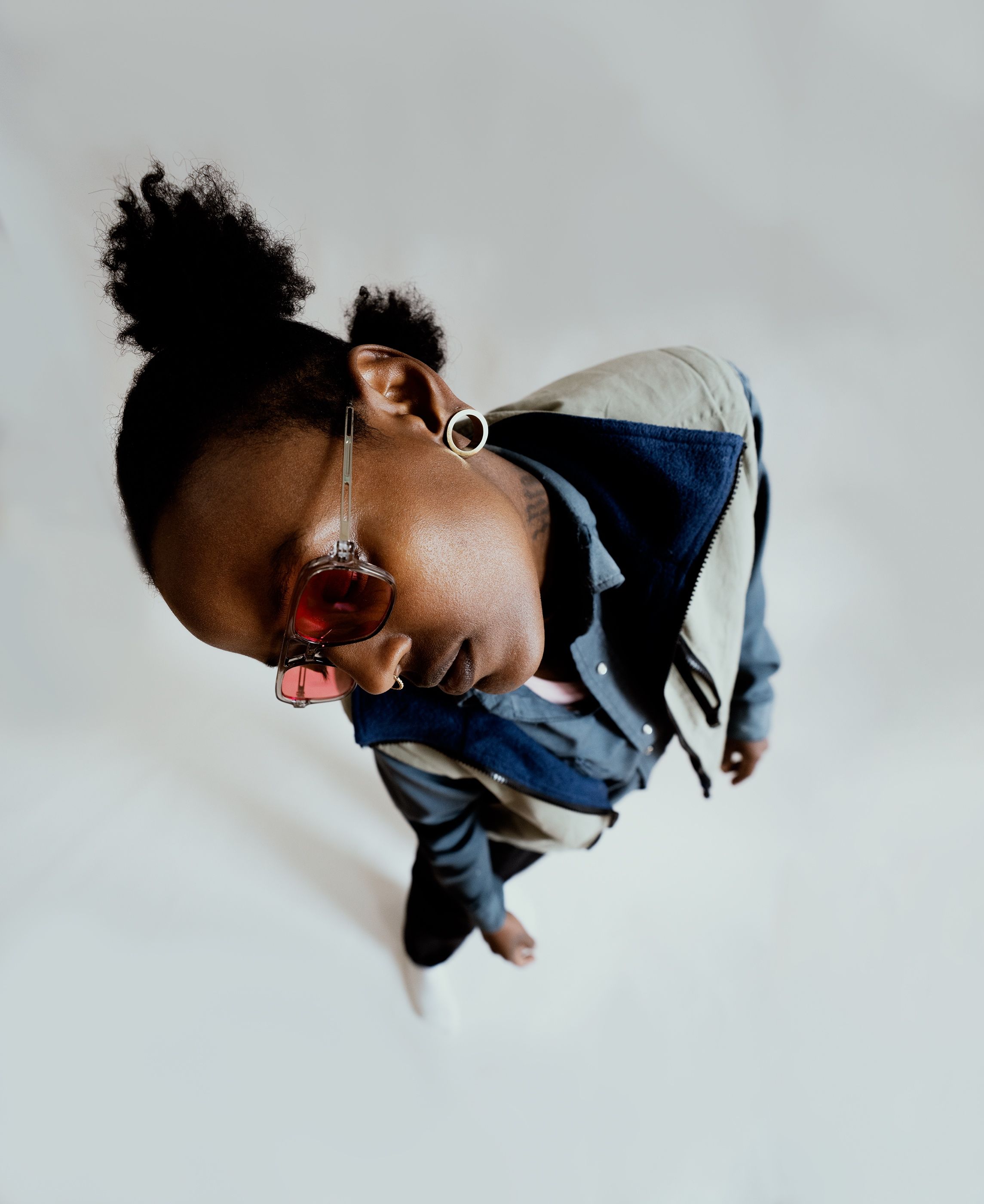 Overhead view of a person with hair in a bun, pink-tinted sunglasses, and a layered jacket.