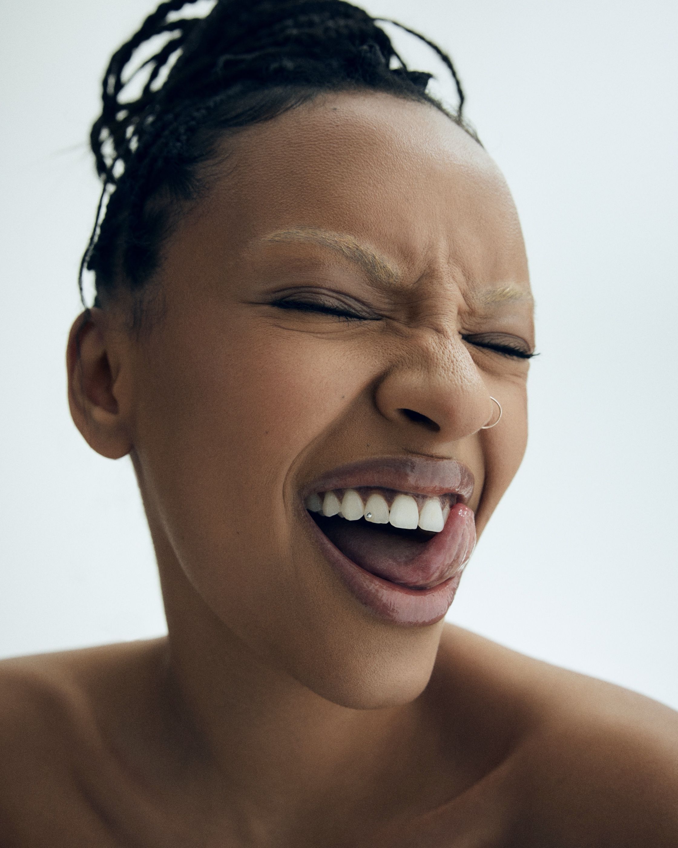 Close-up of a woman laughing with her eyes closed and tongue out, showing a small gem accent on her front tooth.