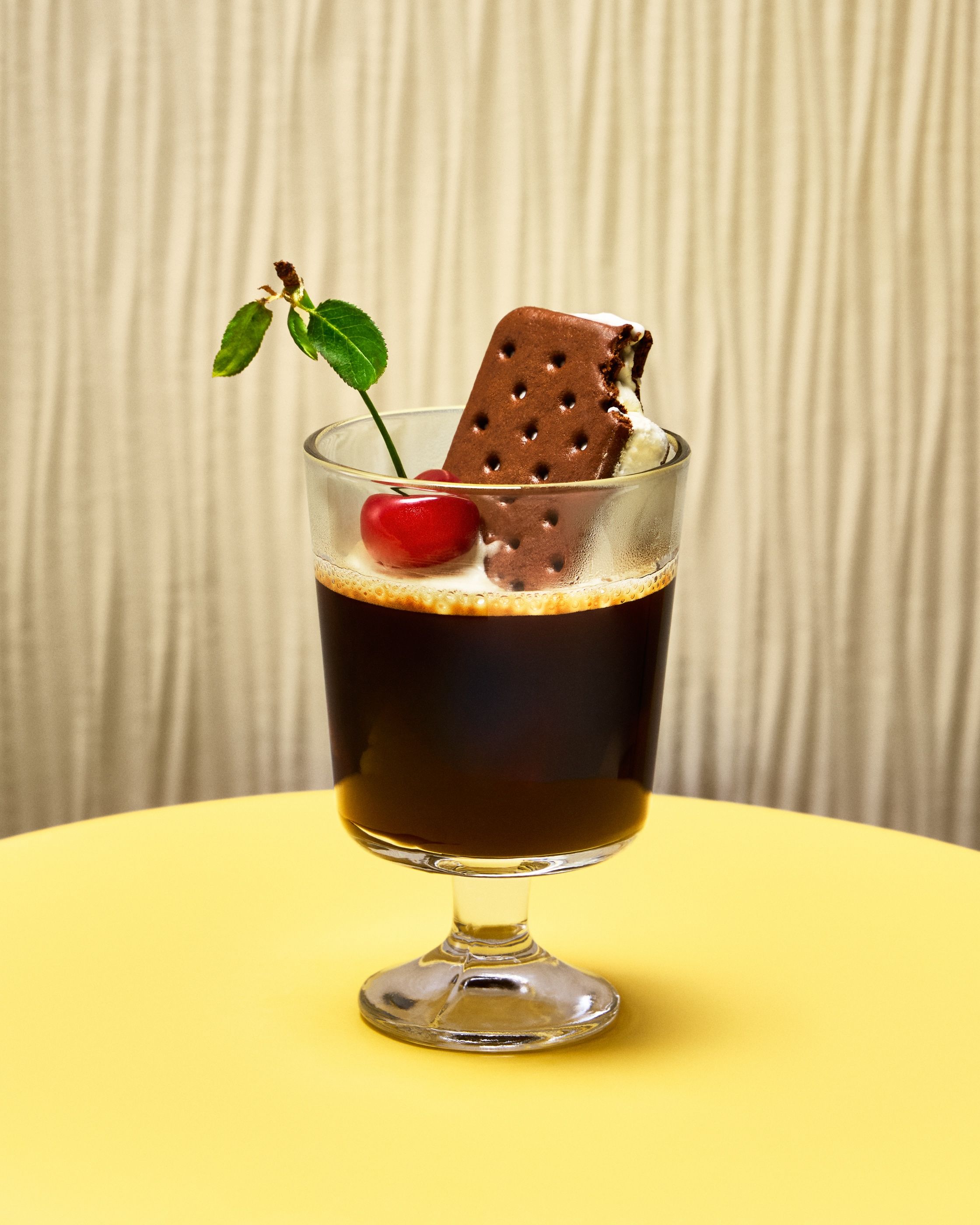 A coffee dessert in a stemmed glass topped with an ice cream sandwich, a cherry, and a mint sprig.