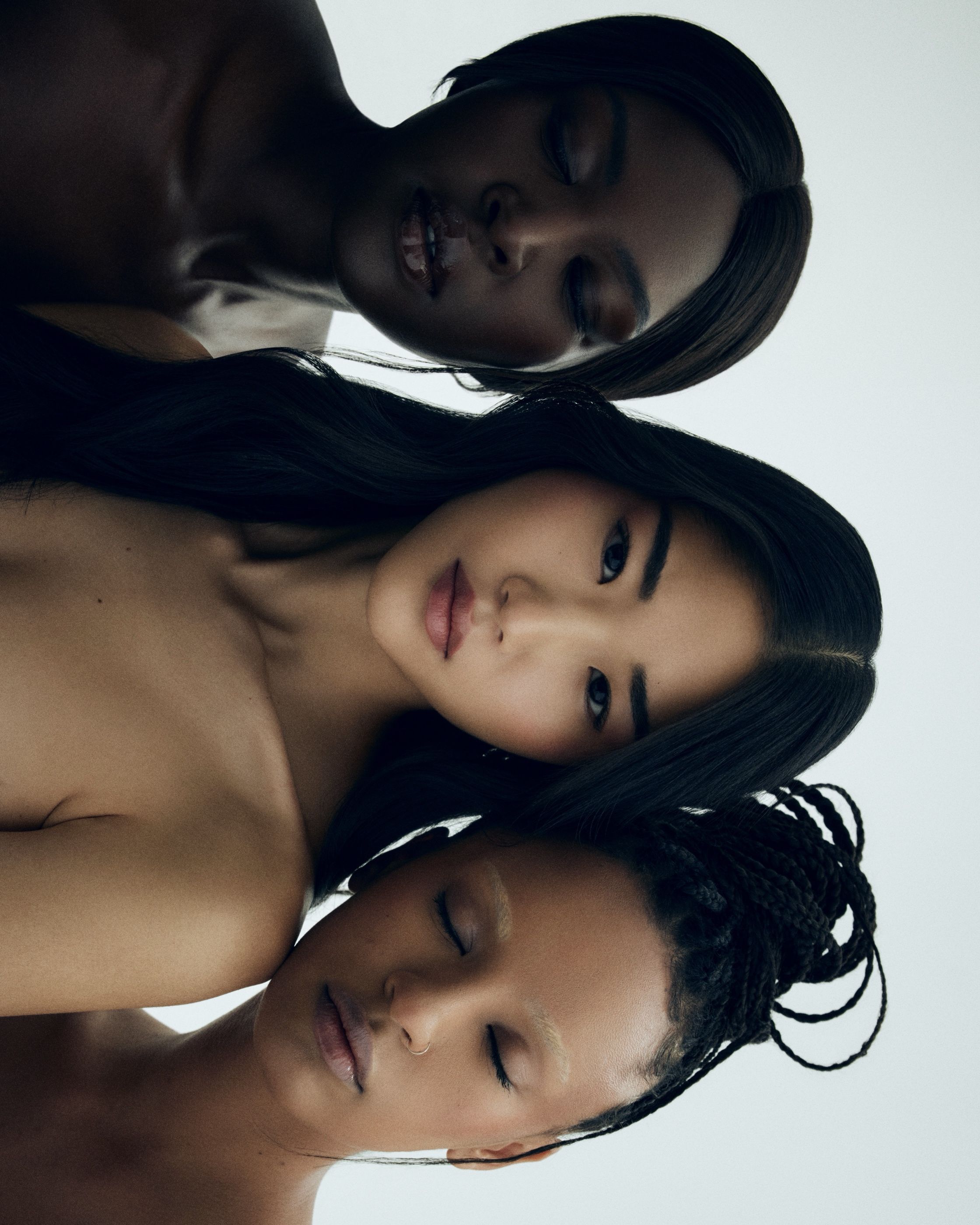 Three women's faces are arranged head to head at different angles, eyes closed, against a white background.